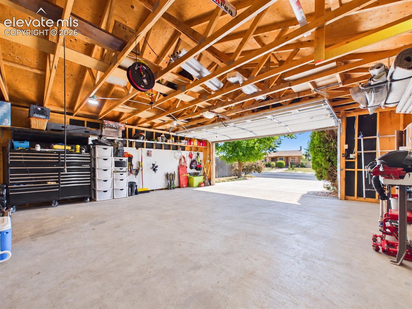 Alternate garage view showcases the generous concrete floor area, exposed framing with overhead storage potential, and organized wall-mounted storage.