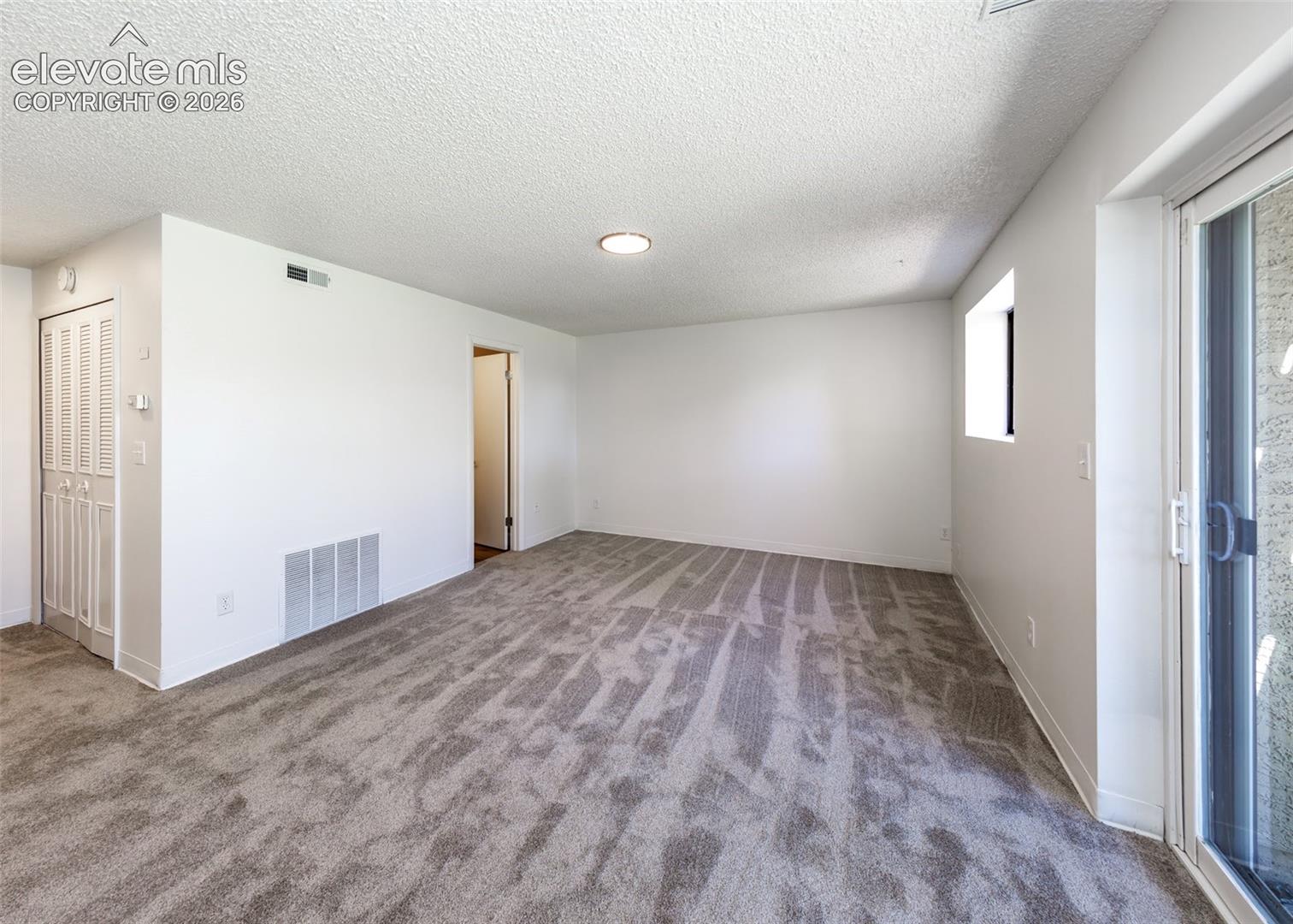 Neutral interior featuring wall-to-wall carpeting, sliding glass doors, built-in closet with bi-fold doors, and a flush-mount light fixture