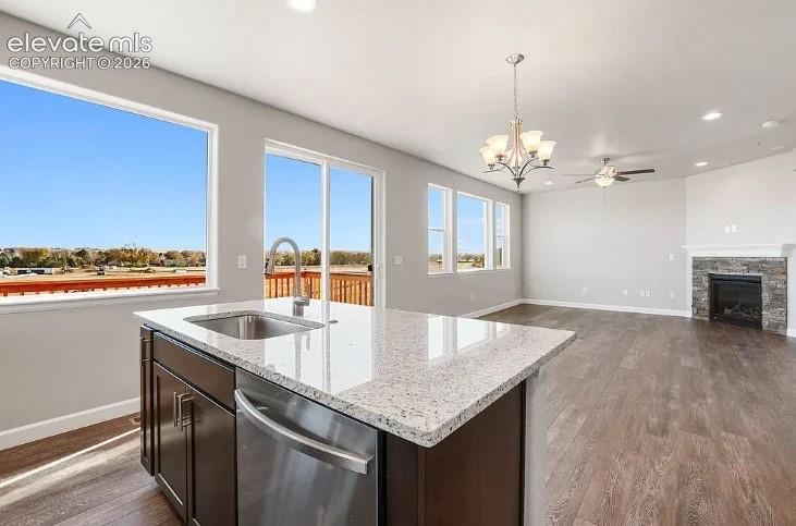 Kitchen island with stone-finish countertop, stainless steel undermount sink, dark-finish cabinetry, recessed lighting, and stone-surround fireplace