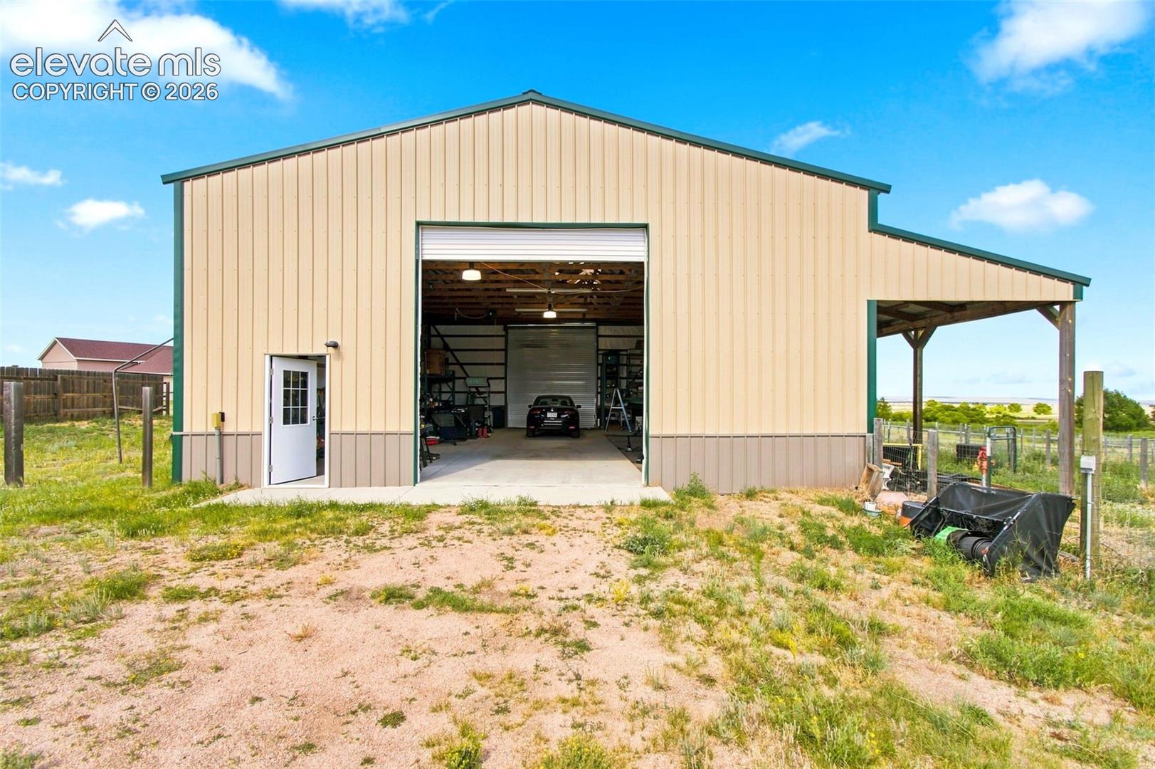Metal-sided outbuilding featuring a large roll-up door, a separate entry door, an attached lean-to, and interior lighting