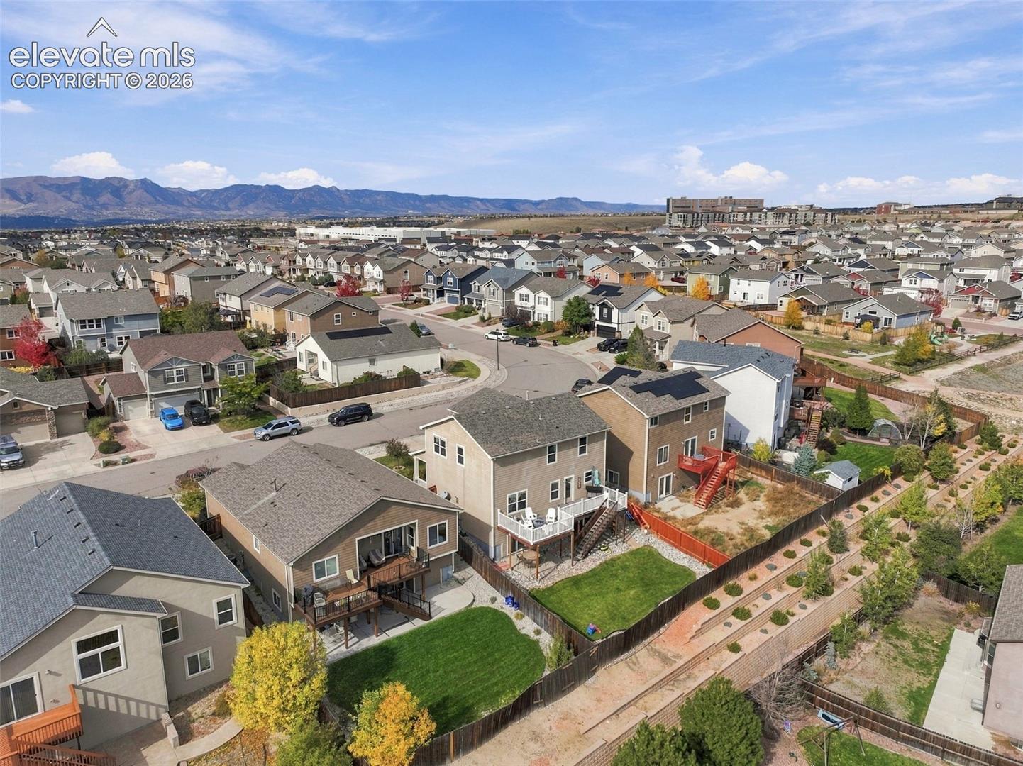 Aerial perspective featuring residential lots with fenced backyards, elevated decks, and mountain scenery