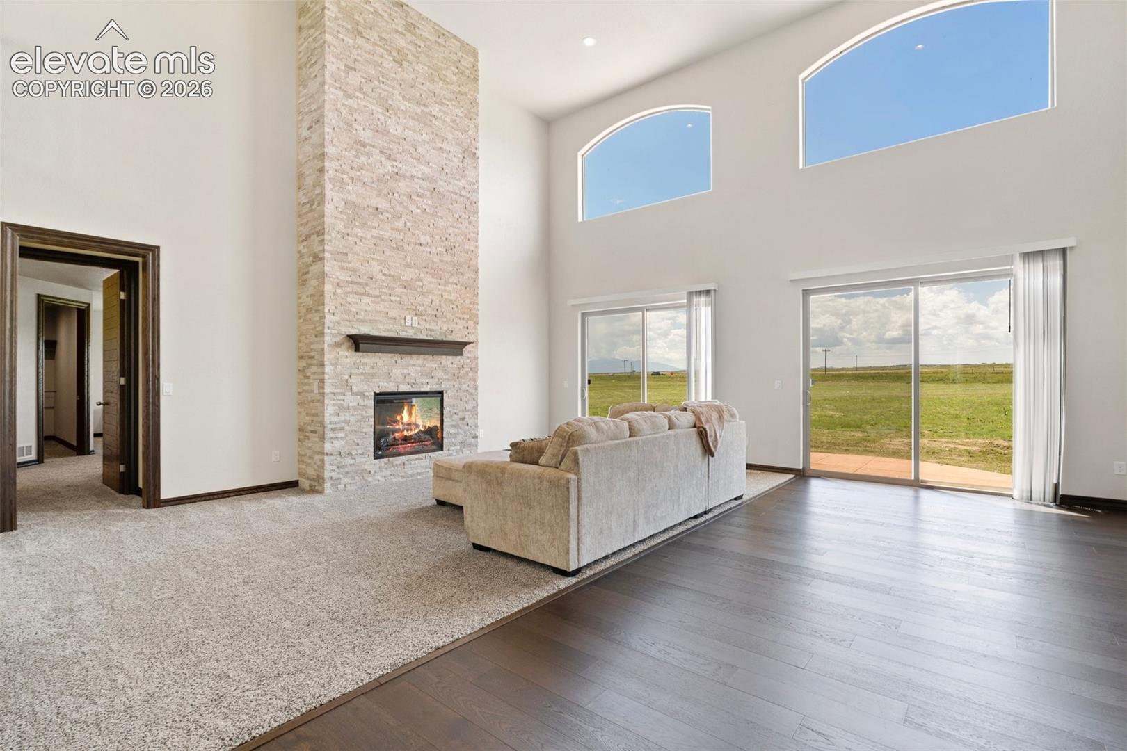 Vaulted living area featuring high arched windows, a stone fireplace, and sliding glass doors to the exterior