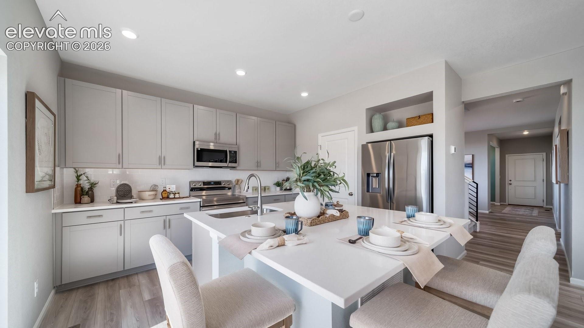 Kitchen featuring light gray cabinetry, stainless steel appliances, a white tile backsplash, and a central island with a white countertop and integrated seating
*photos of a model home*