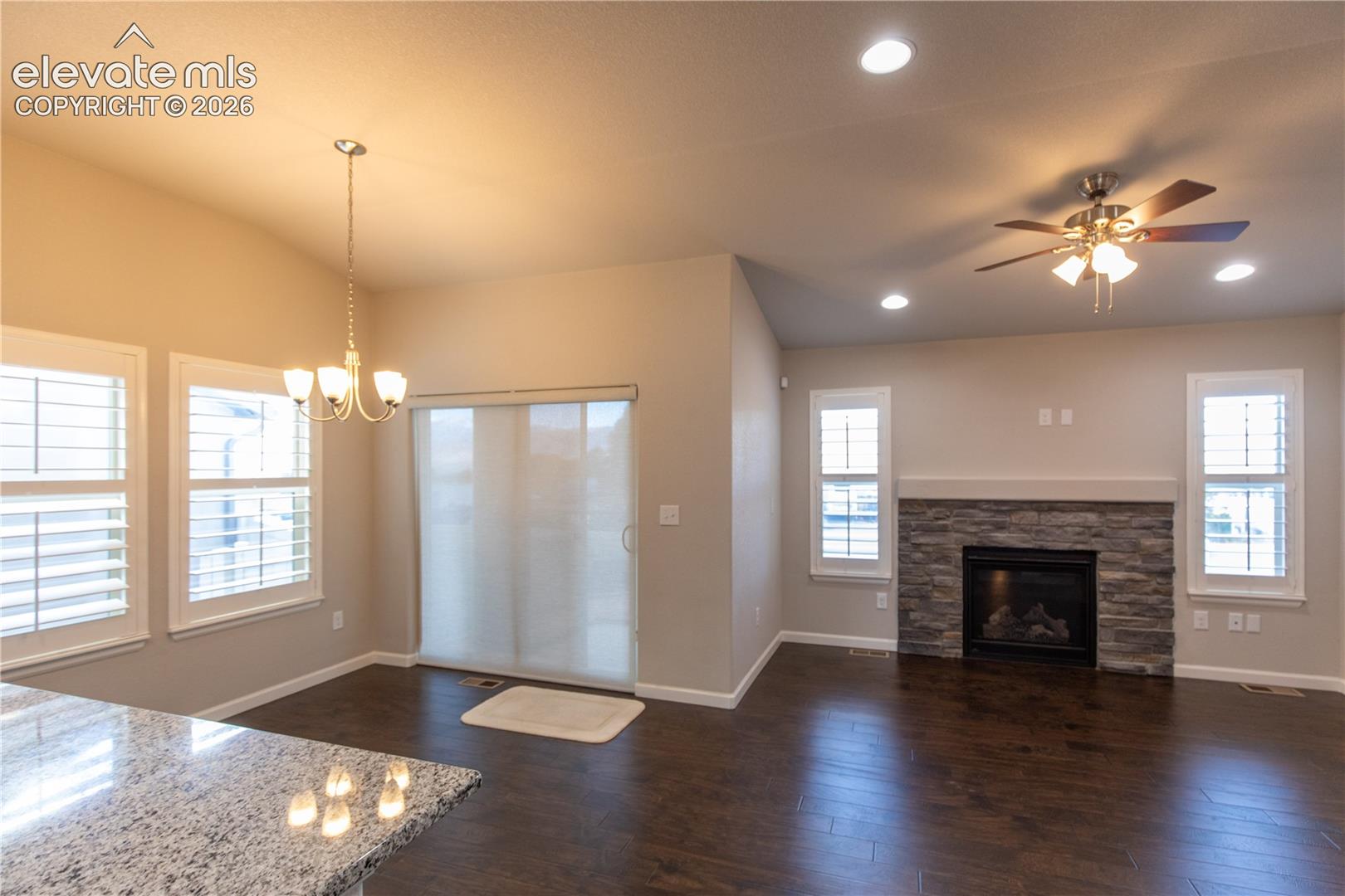 Open-concept area featuring stone-surround fireplace, wood-finish flooring, recessed lighting, plantation shutters, and sliding glass door
