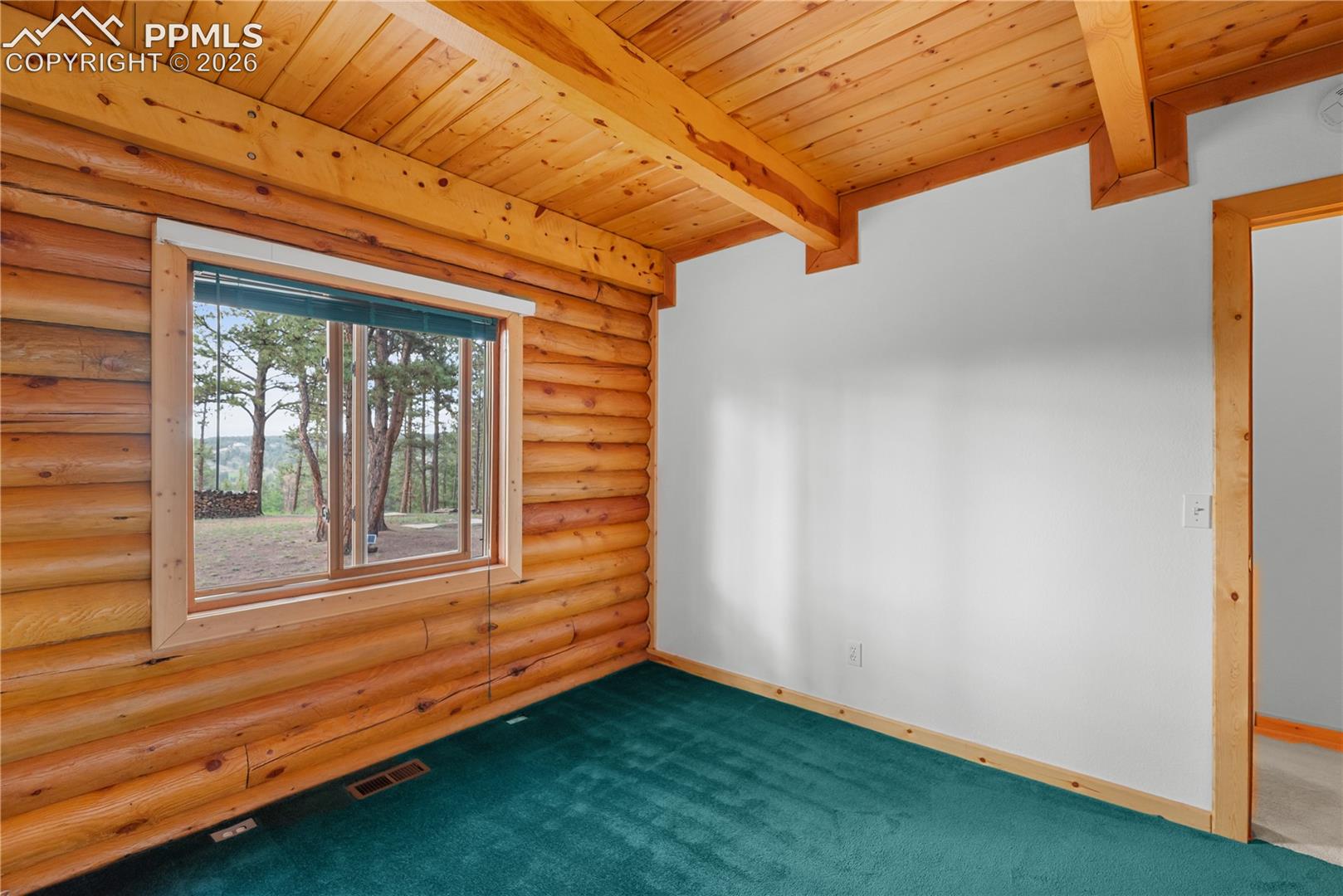 Empty room featuring rustic walls, a wood ceiling with exposed beams, and dark colored carpet