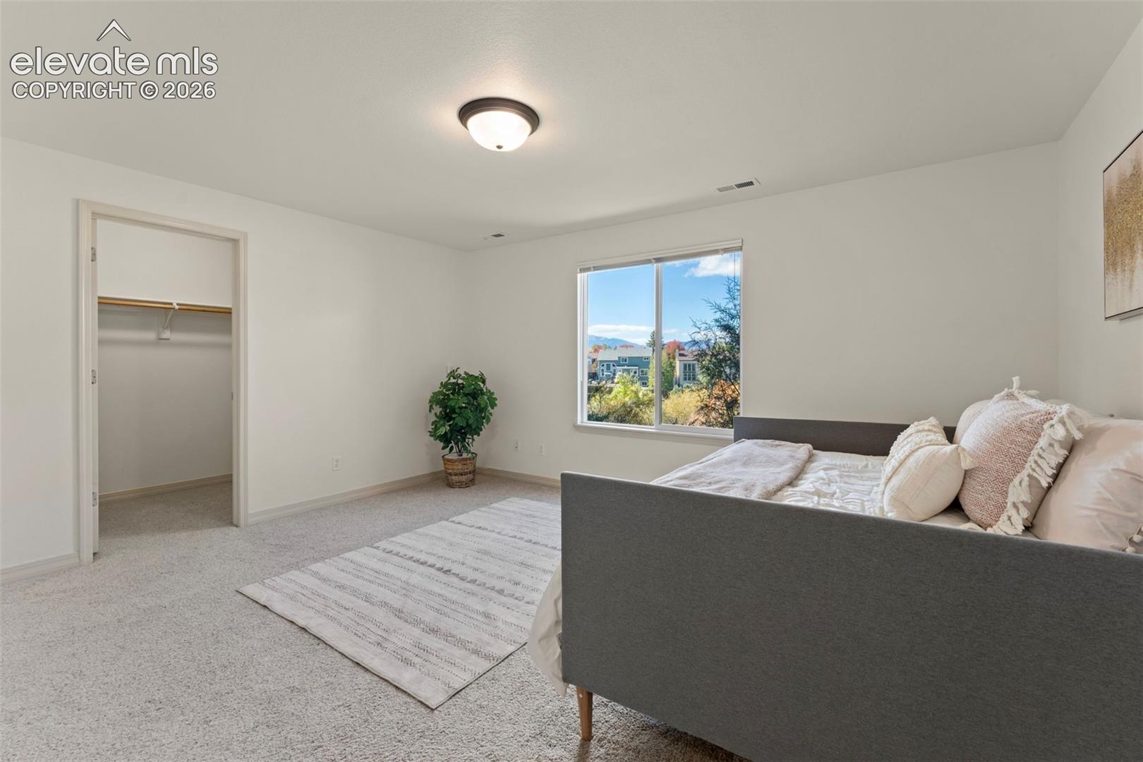 Neutral-toned carpeting, flush-mount ceiling lighting, sliding window, and walk-in closet with built-in shelving