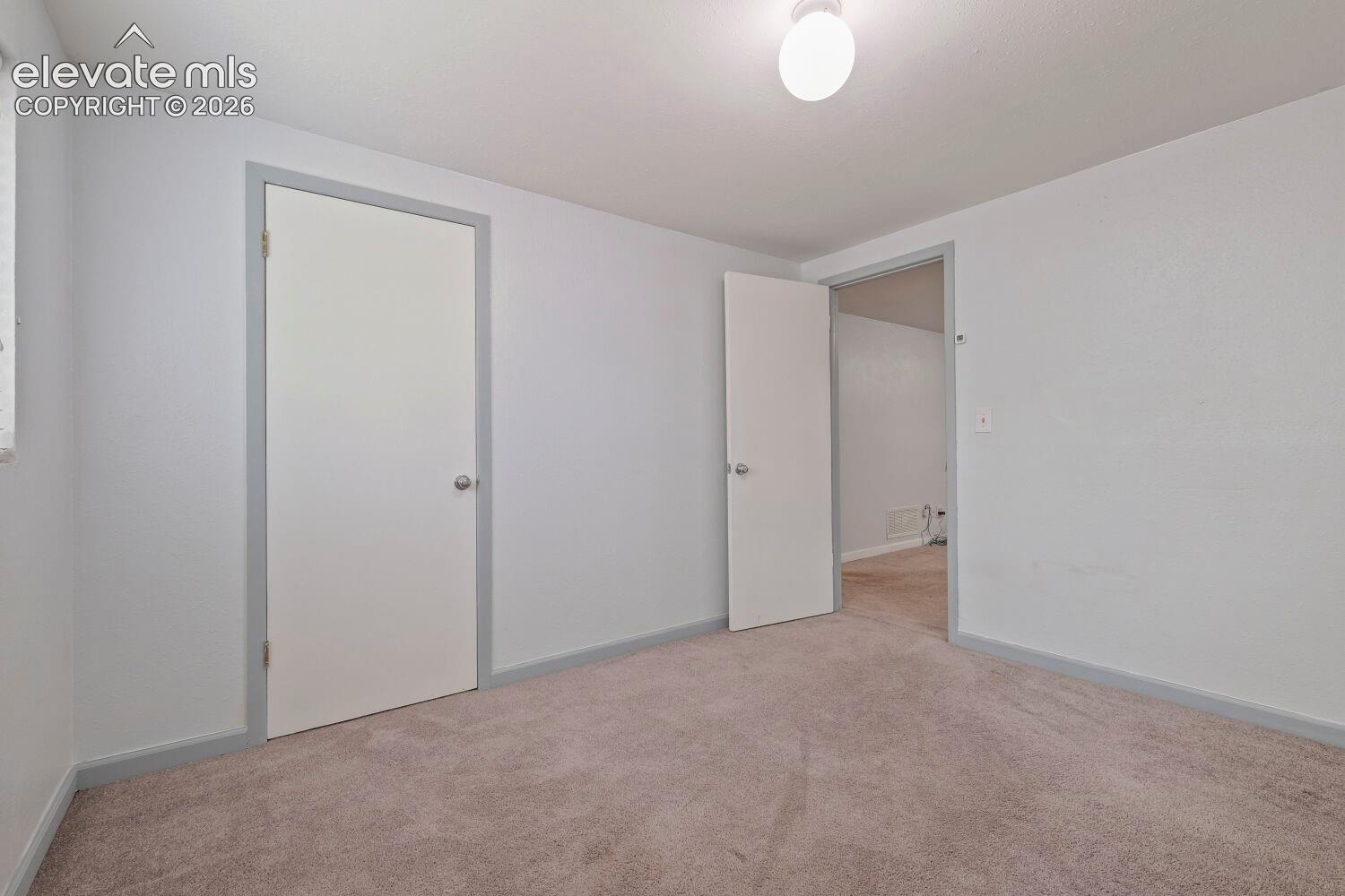Carpeted interior space featuring light gray walls, white trim, and a flush mount ceiling light fixture
