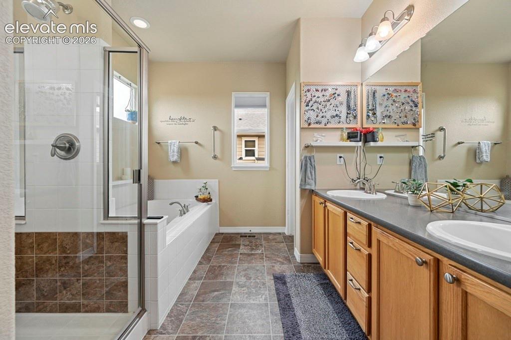 Dual vanity with integrated sinks, wood-finish cabinetry, a glass-enclosed shower, a built-in bathtub, and tile flooring