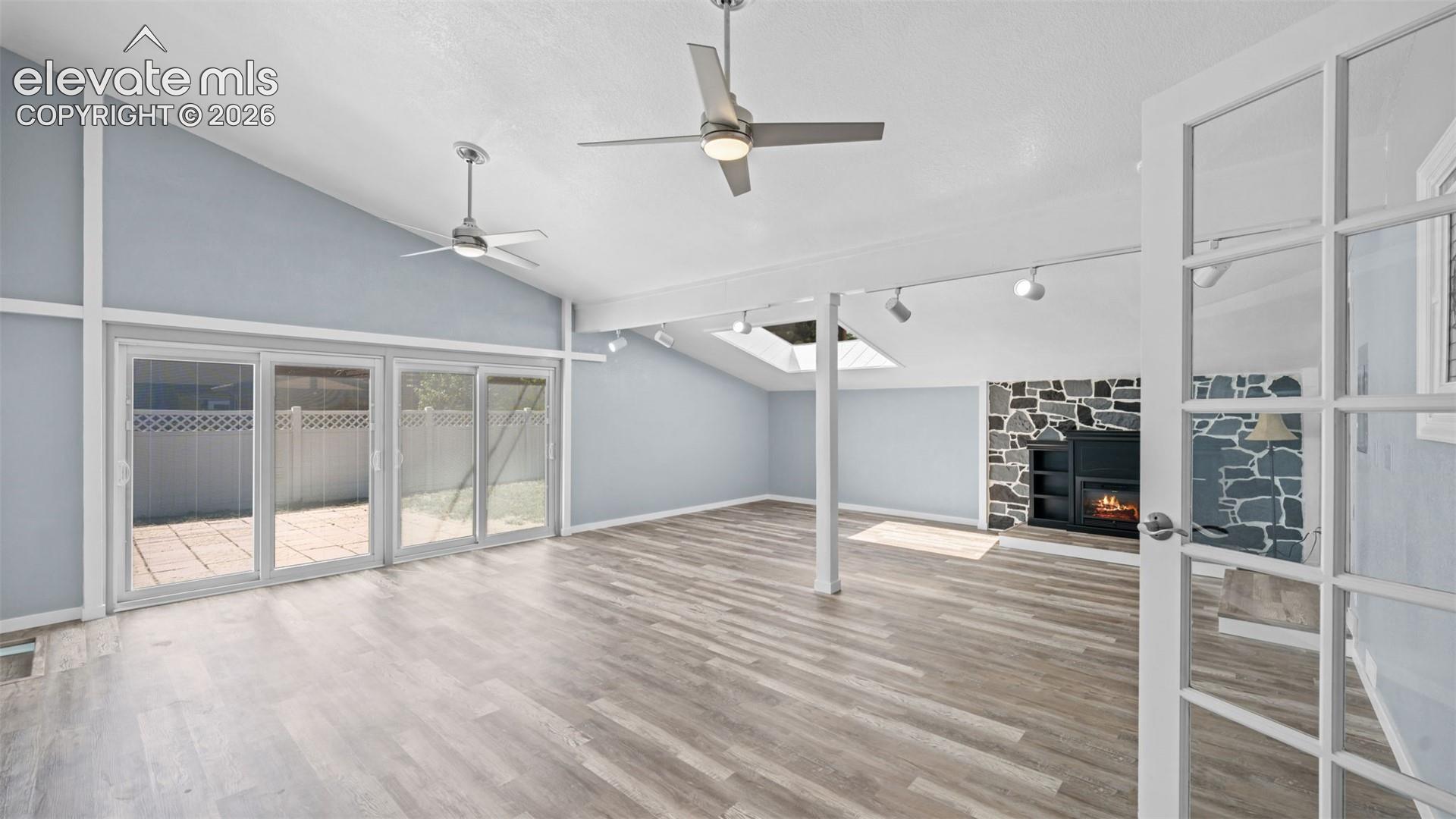 Spacious living area featuring wood-finish flooring, vaulted ceilings with ceiling fans, and a stone-faced fireplace with built-in shelving