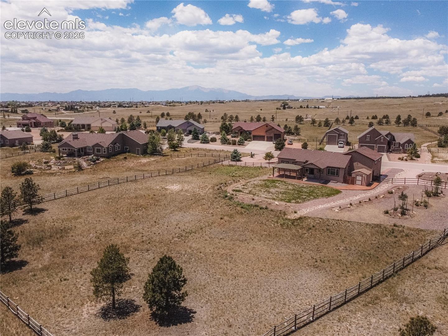 Expansive property featuring a brown ranch-style home with a covered front porch, a detached shed, a paved driveway, and an open field surrounded by fencing