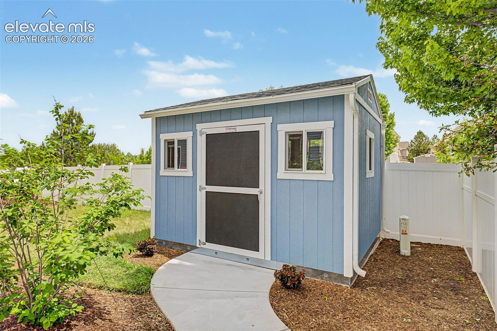 A substantial storage shed with windows and a ramp sits neatly in the corner of the fenced yard, adding the kind of practical outdoor storage that every homeowner appreciates.
