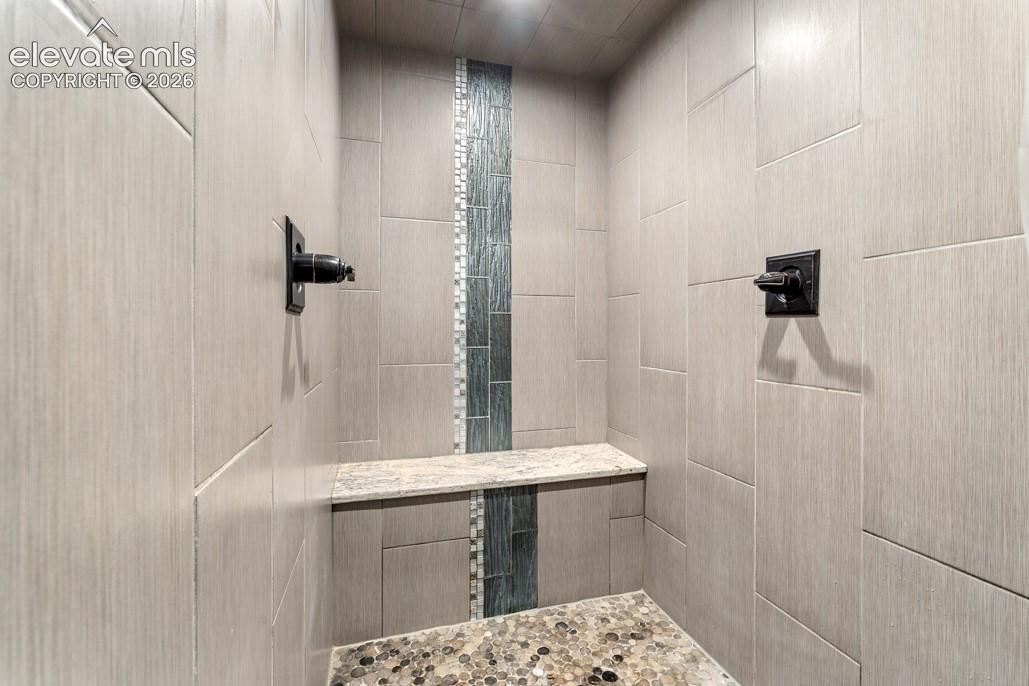 Walk-in shower featuring large format tile, a decorative vertical accent tile, a built-in bench, and a river rock shower floor