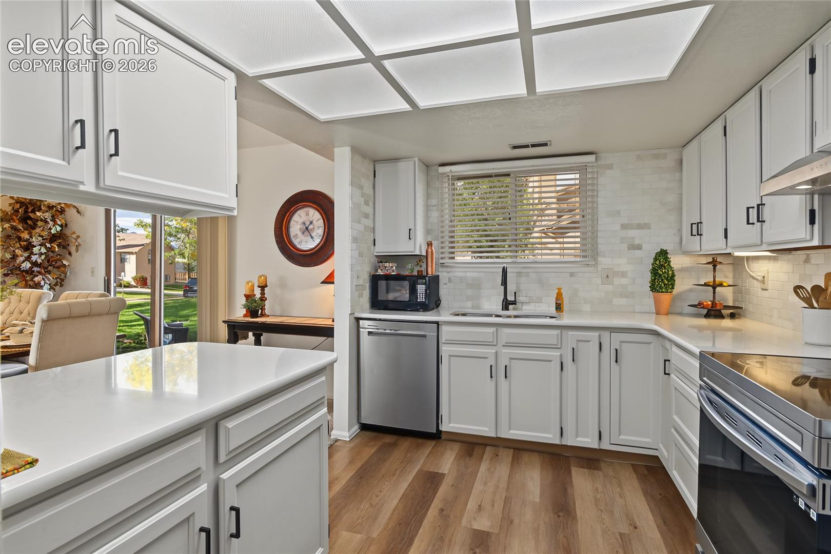 Kitchen featuring white shaker-style cabinetry, stainless steel appliances, wood-finish flooring, white countertops, and a subway tile backsplash