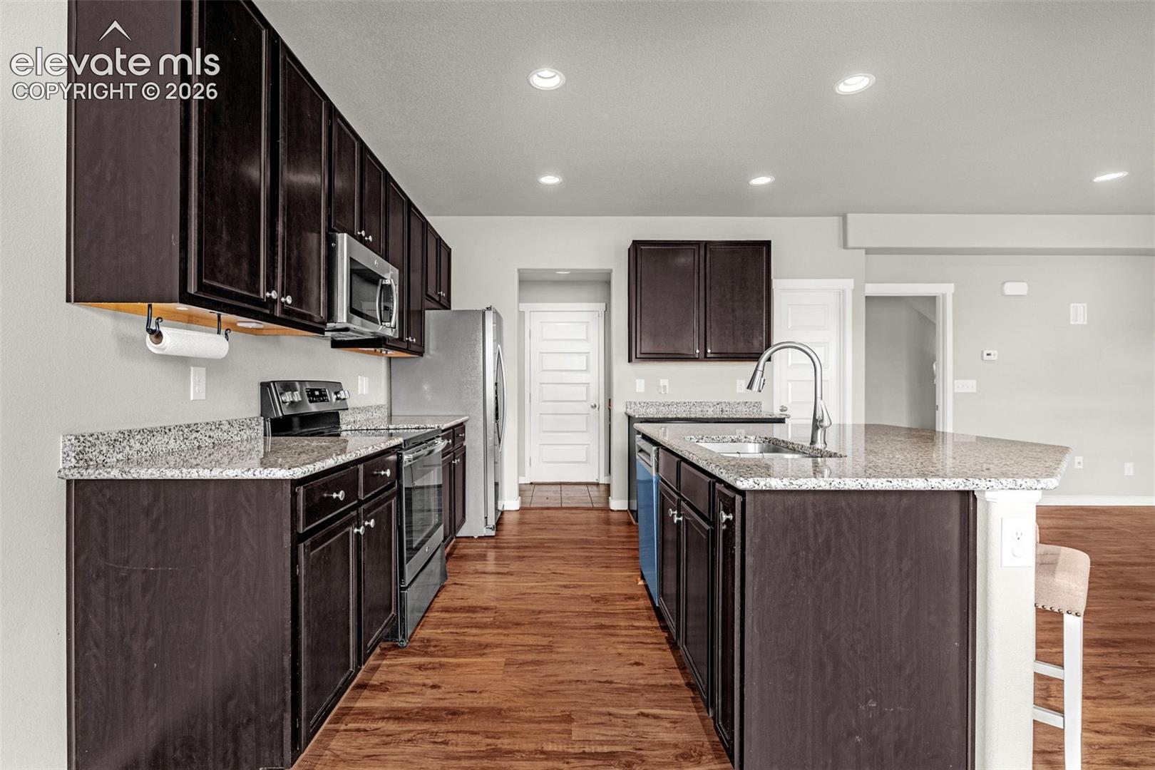 Kitchen featuring wood-finish flooring, dark wood cabinetry, granite countertops, and stainless steel appliances
