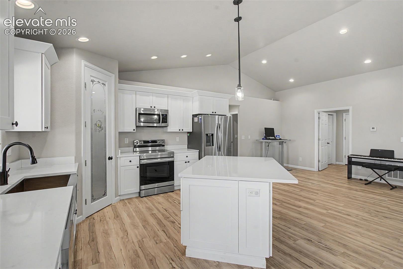Spacious kitchen featuring white cabinetry, stainless steel appliances, a center island with countertop seating, and wood-finish flooring