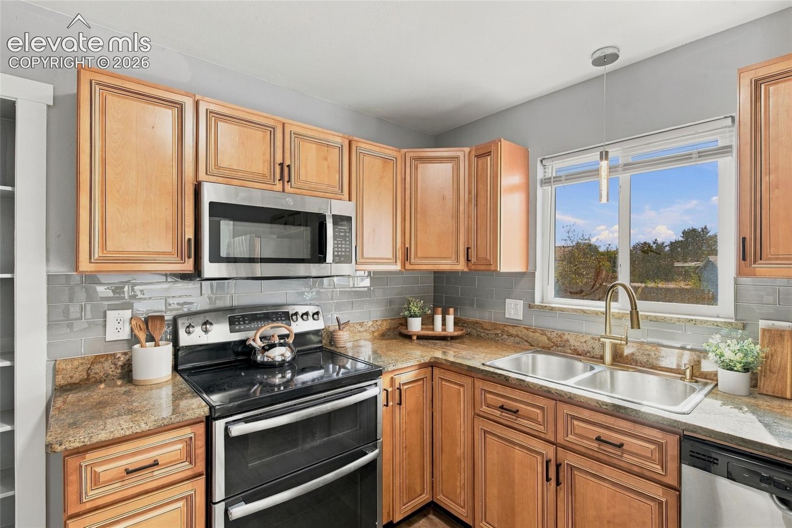 Kitchen featuring natural wood cabinetry, stone-finish countertops, subway tile backsplash, stainless steel appliances, and an undermount dual-basin sink with a gooseneck faucet