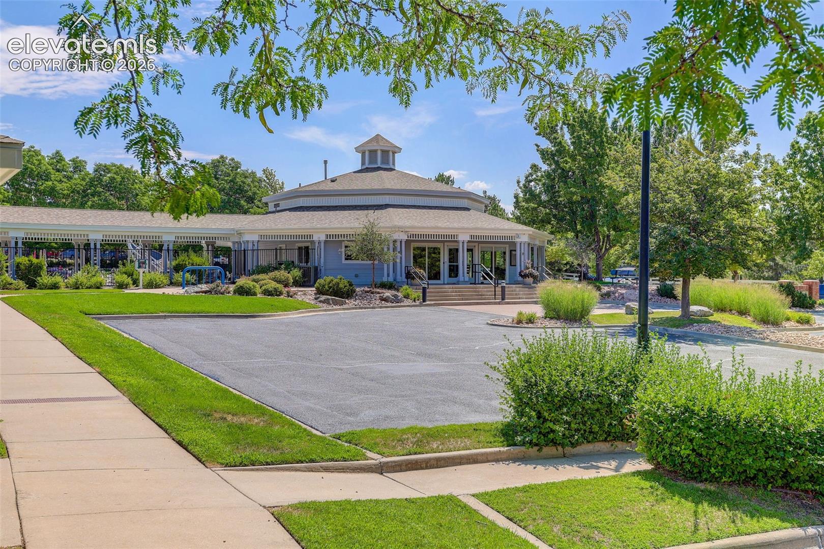 Circular Clubhouse building with a cupola, surrounded by landscaped grounds, a paved parking area, and mature trees