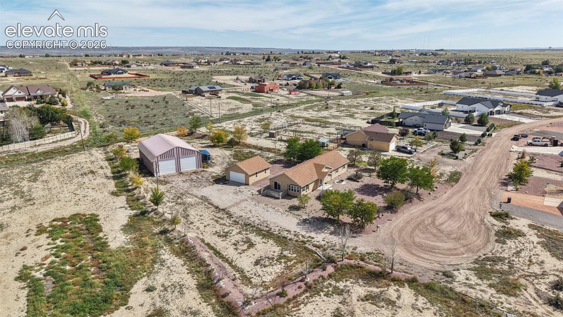 Aerial perspective featuring a single-level residence, a detached garage, and a separate metal-sided outbuilding situated on a large-acreage lot