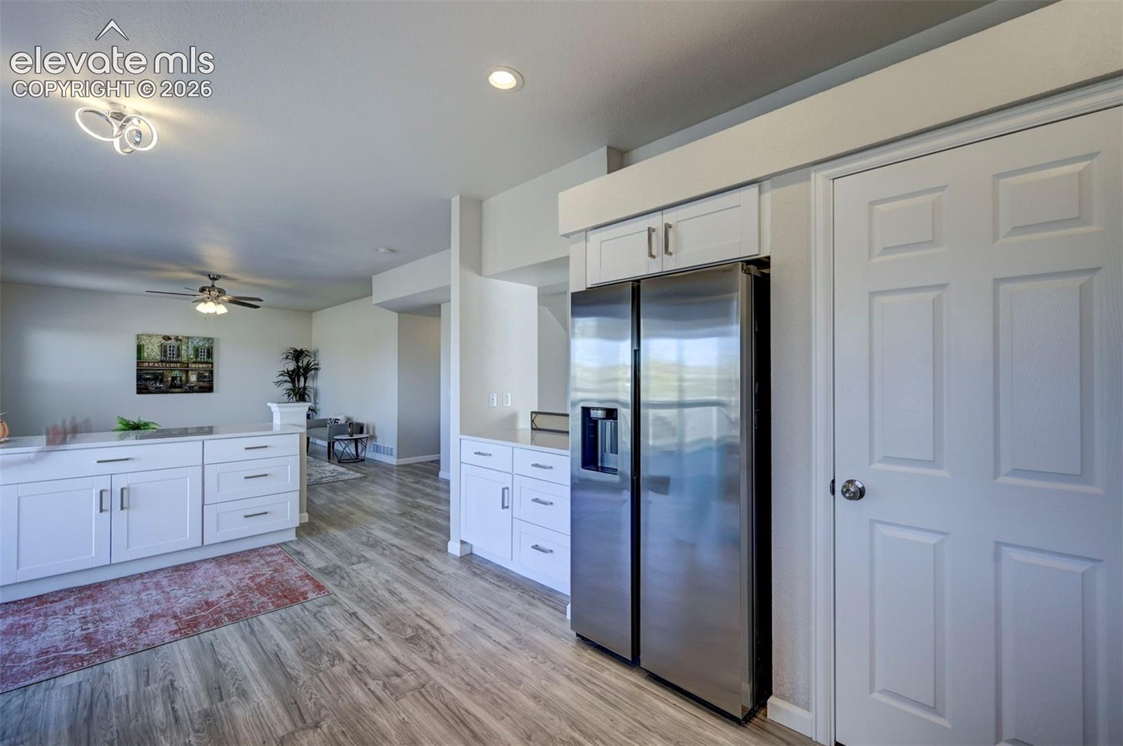 White cabinetry with brushed nickel pulls, stainless steel side-by-side refrigerator, wood-finish flooring, recessed lighting, and six-panel interior door