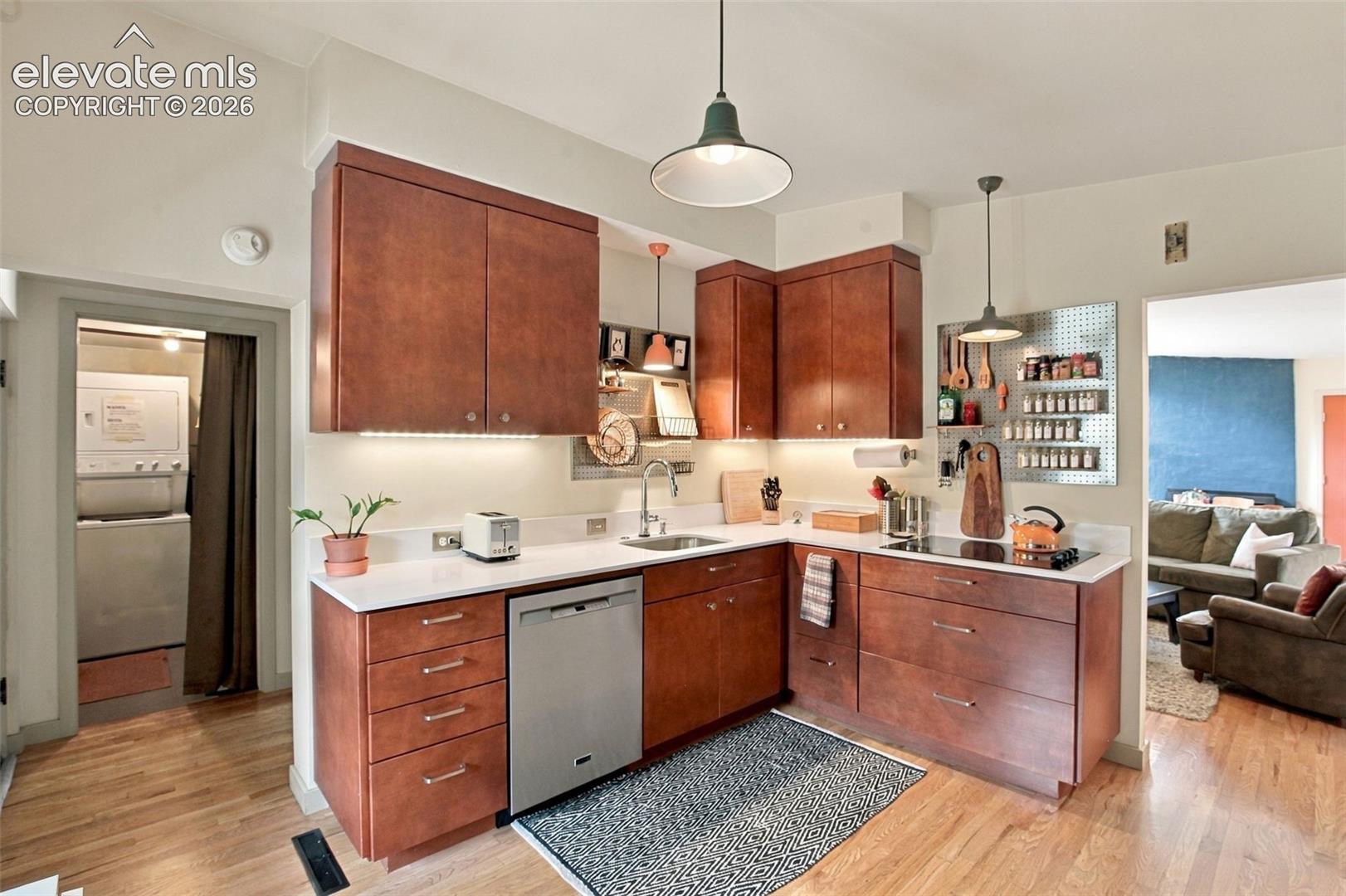 Kitchen featuring wood-finish cabinetry, solid surface countertops, stainless steel dishwasher, and dual pendant lighting, complete with hardwood flooring