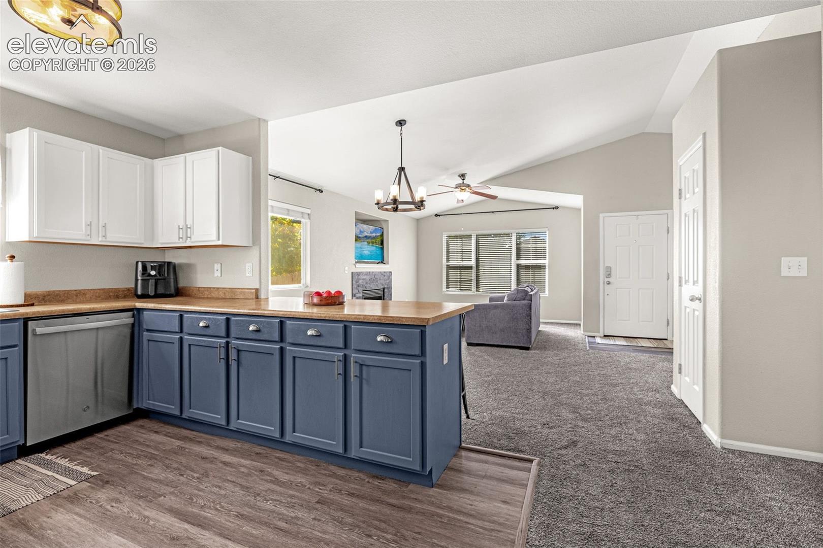 Open-concept living area featuring vaulted ceilings, wood-finish flooring, a kitchen island with storage, stainless steel dishwasher, and built-in ceiling fans