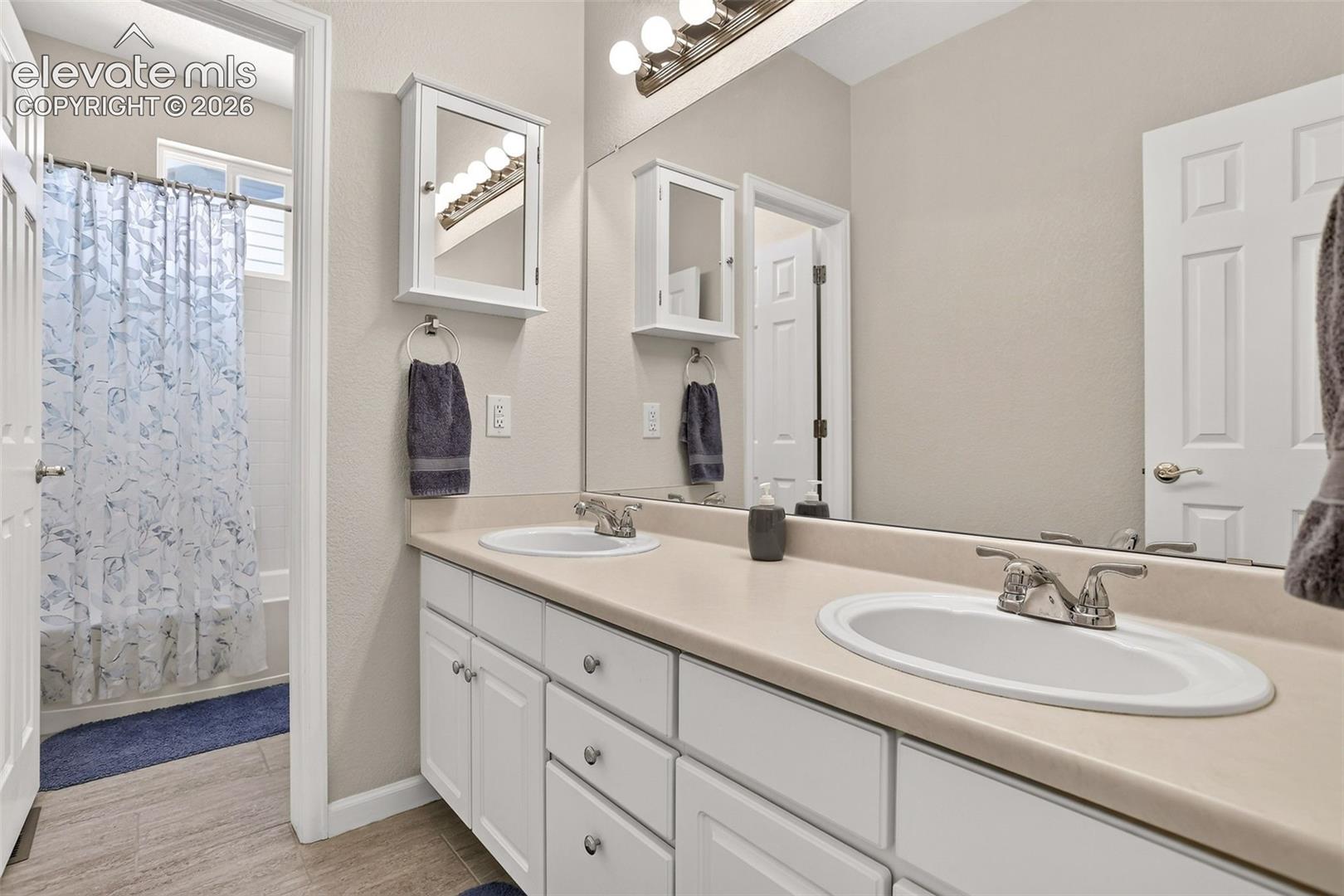 Dual vanity with integrated sinks, white cabinetry, full-width mirror, and wall-mounted vanity light fixture