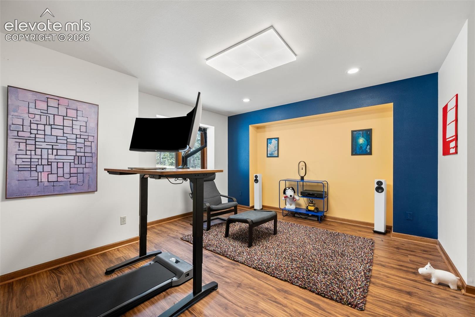 Spacious room featuring wood-finish flooring, recessed lighting, and a large ceiling-mounted light panel