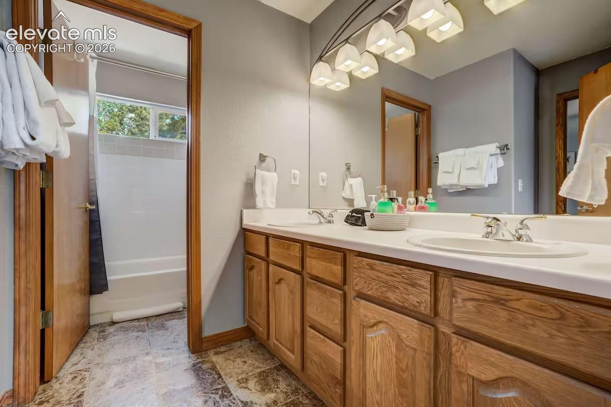 Bathroom featuring a dual-sink vanity with wood cabinetry, a large mirror, and overhead lighting