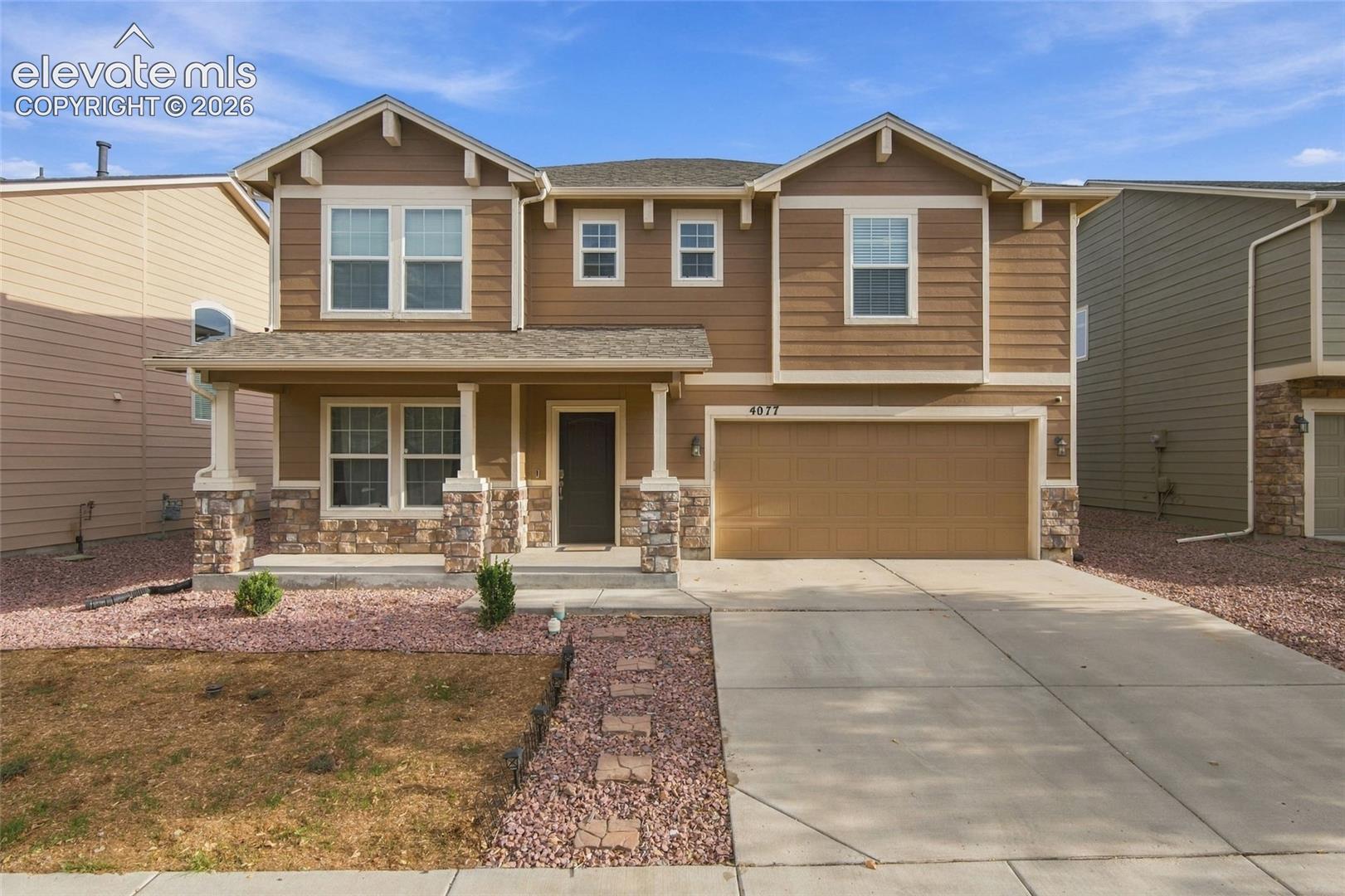 Two-story exterior featuring lap siding, stone veneer accents, a covered front porch with decorative columns, and an attached two-car garage