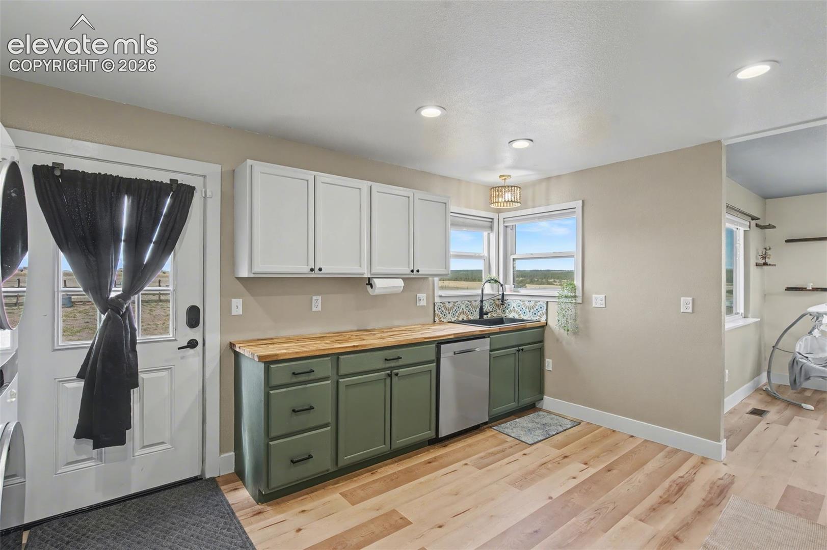Kitchen featuring two-tone cabinetry with matte black hardware, wood-finish countertops, stainless steel dishwasher, undermount sink, and wood-finish flooring