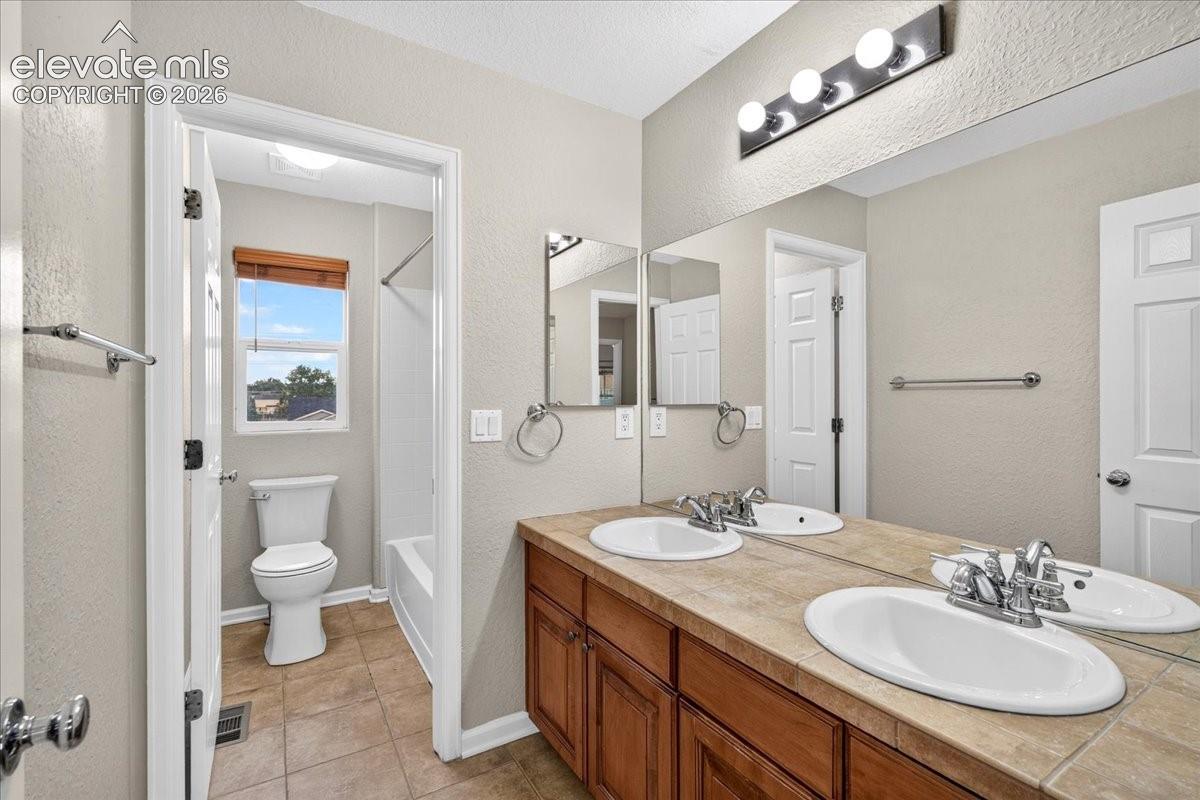 Dual vanity with integrated sinks, wood-finish cabinetry, tile countertop, and a full-width mirror