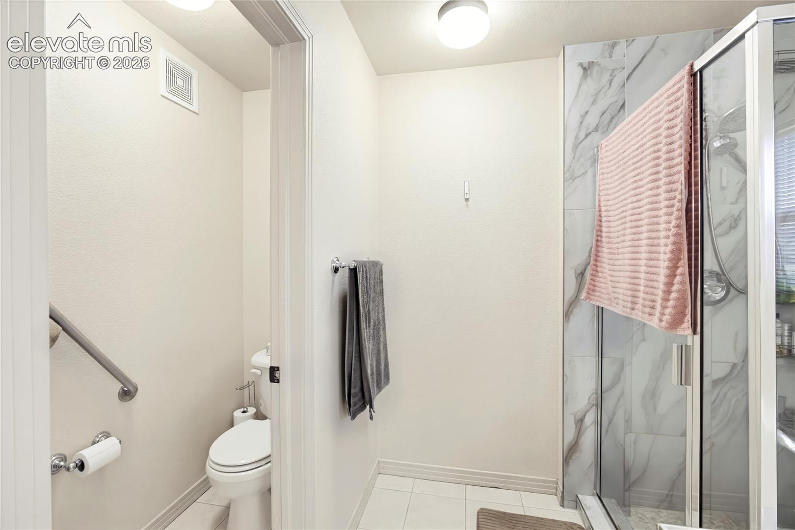 Glass-enclosed shower with a tiled surround, grab bar, and white toilet