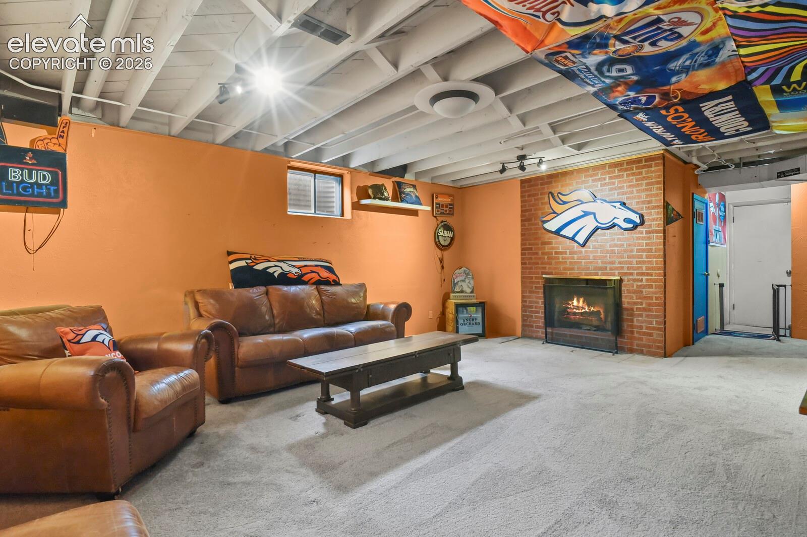 Lower level room featuring brick-surround fireplace, exposed beam ceiling, track lighting, and carpeted flooring
