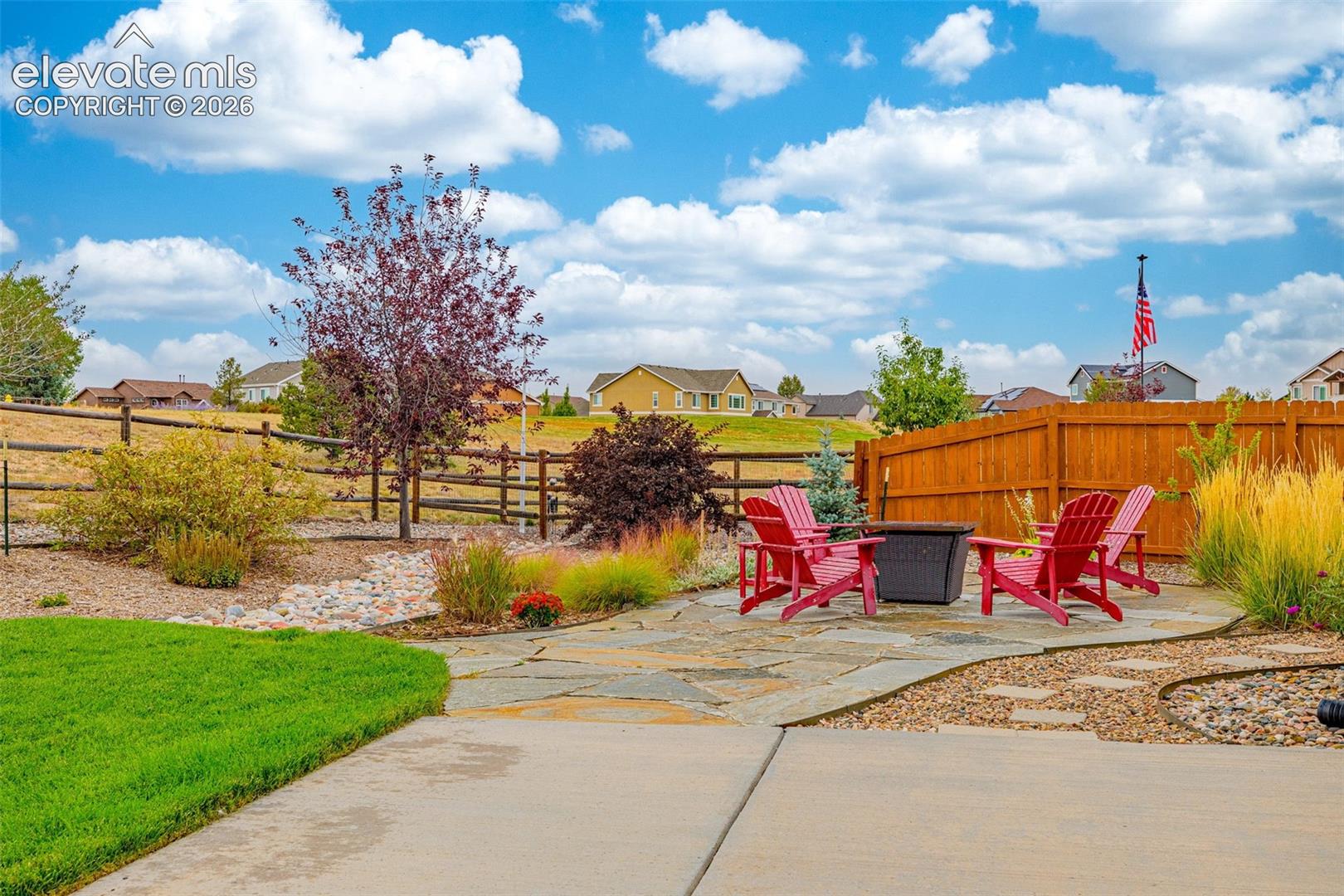 Backyard featuring a flagstone patio, wood privacy fencing, a split-rail rear perimeter fence, and xeriscaped garden beds with ornamental grasses
