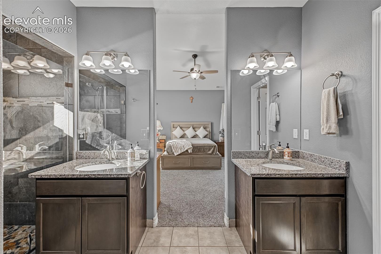Walk-in shower with dark tile surround and stone flooring, stone-topped dual vanities vanity with undermount sinks and a walk-in closet. 