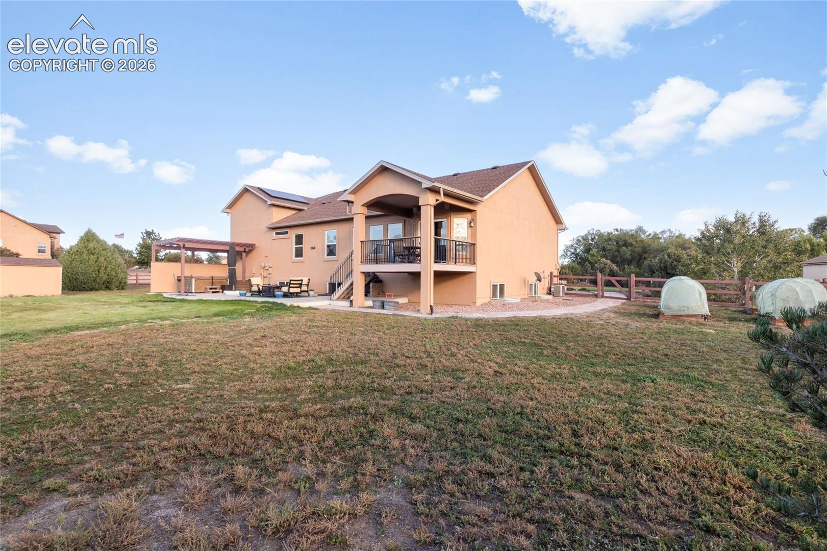 Back of the home, mostly natural grass with some lawn, raised garden beds, covered deck off the breakfast area, hot tub with pergola