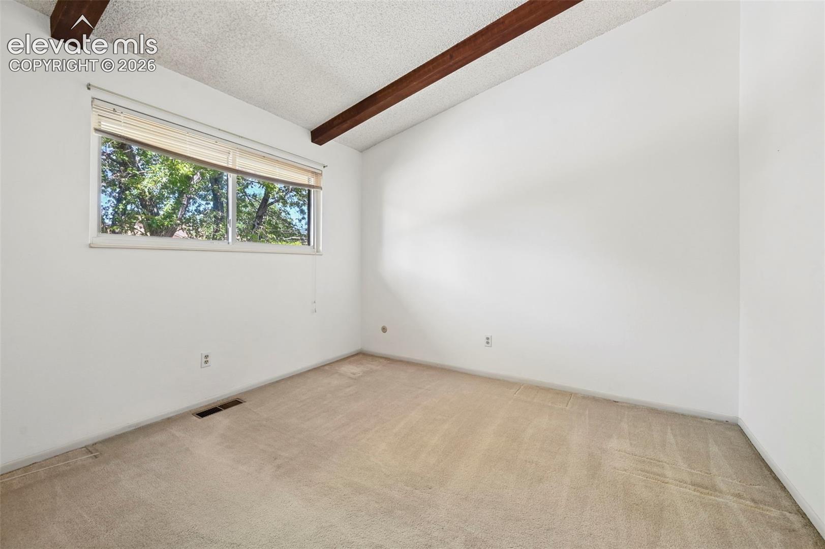 Vaulted ceiling with exposed wood beams, wall-to-wall carpeting, and a double-paned window