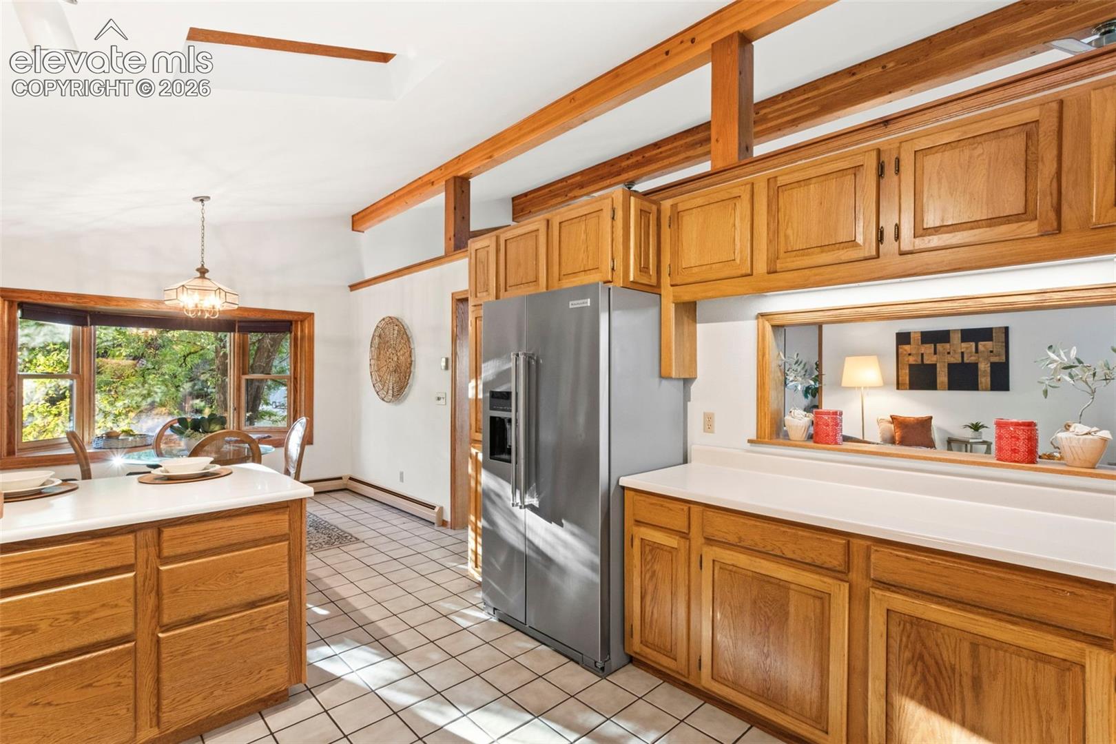 Kitchen featuring wood cabinetry, stainless steel refrigerator, white countertops, ceramic tile flooring, and exposed ceiling beams with a built-in skylight