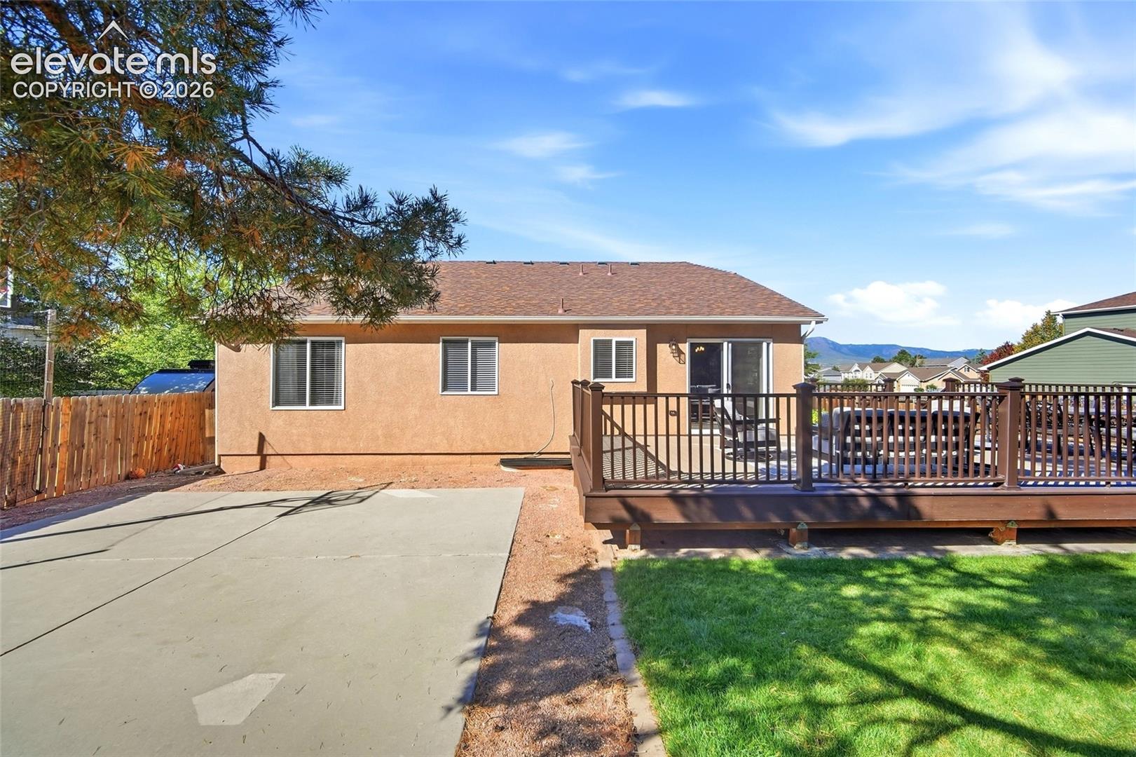 Spacious rear exterior featuring an expansive wood-finish deck with railings, sliding glass door access, a concrete patio area, and a fenced perimeter