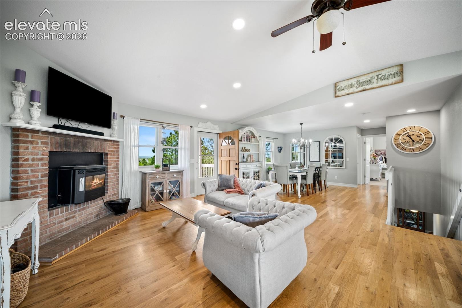 Open-concept living area featuring wood-finish flooring, a brick-surround fireplace with a white mantel, recessed lighting, and a ceiling fan