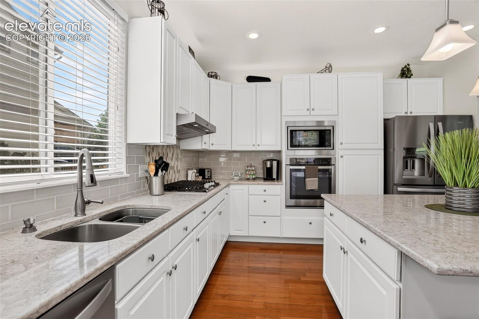 Kitchen featuring white cabinetry, light-toned countertops, stainless steel appliances, wood-finish flooring, and a subway tile backsplash