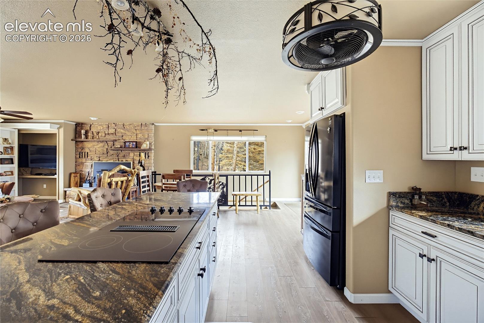 Kitchen featuring white cabinetry, dark stone countertops, an integrated cooktop, and wood-finish flooring, complemented by a floor-to-ceiling stone fireplace