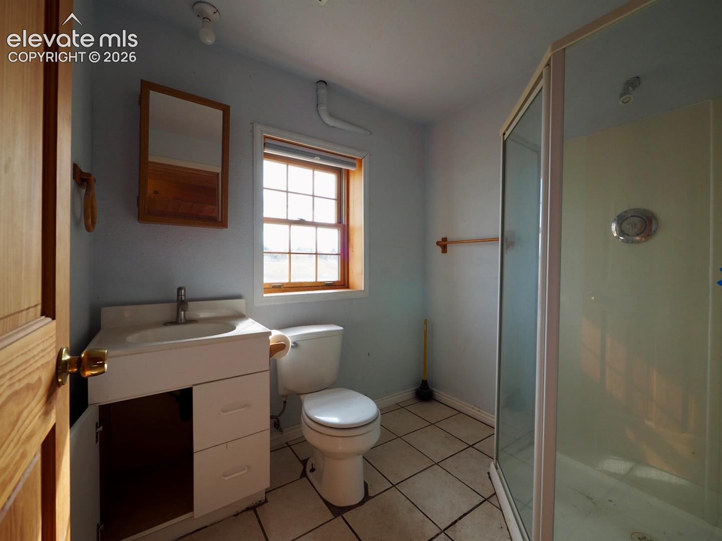Bathroom featuring a corner shower enclosure, vanity with an integrated sink, multi-pane window, and tile flooring