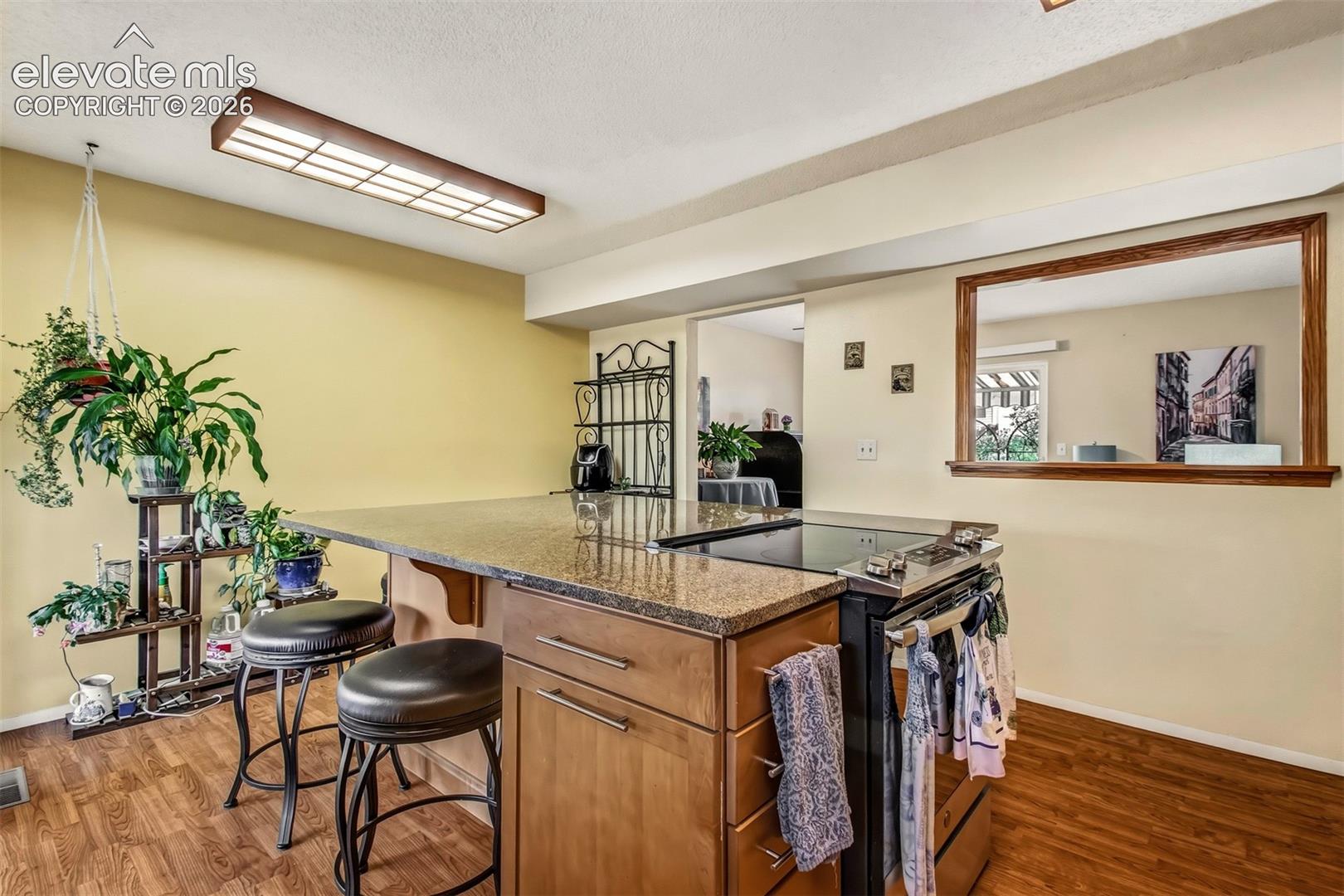 Kitchen island featuring stone countertop, integrated cooktop, wood-finish cabinetry, and overhead linear lighting