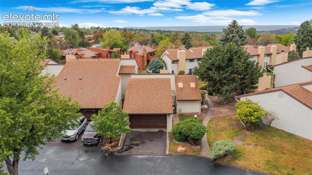 Townhome exterior featuring a brown shingle roof, attached garage, and mature landscaping
