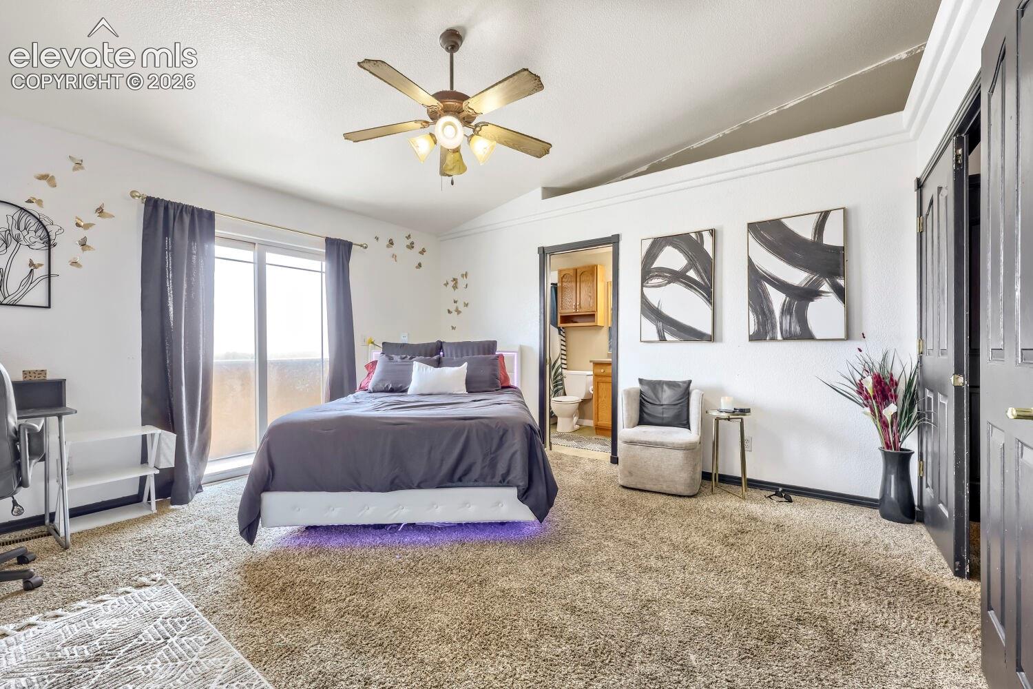 Carpeted room featuring a vaulted ceiling with a ceiling fan, sliding glass door, and an attached bathroom