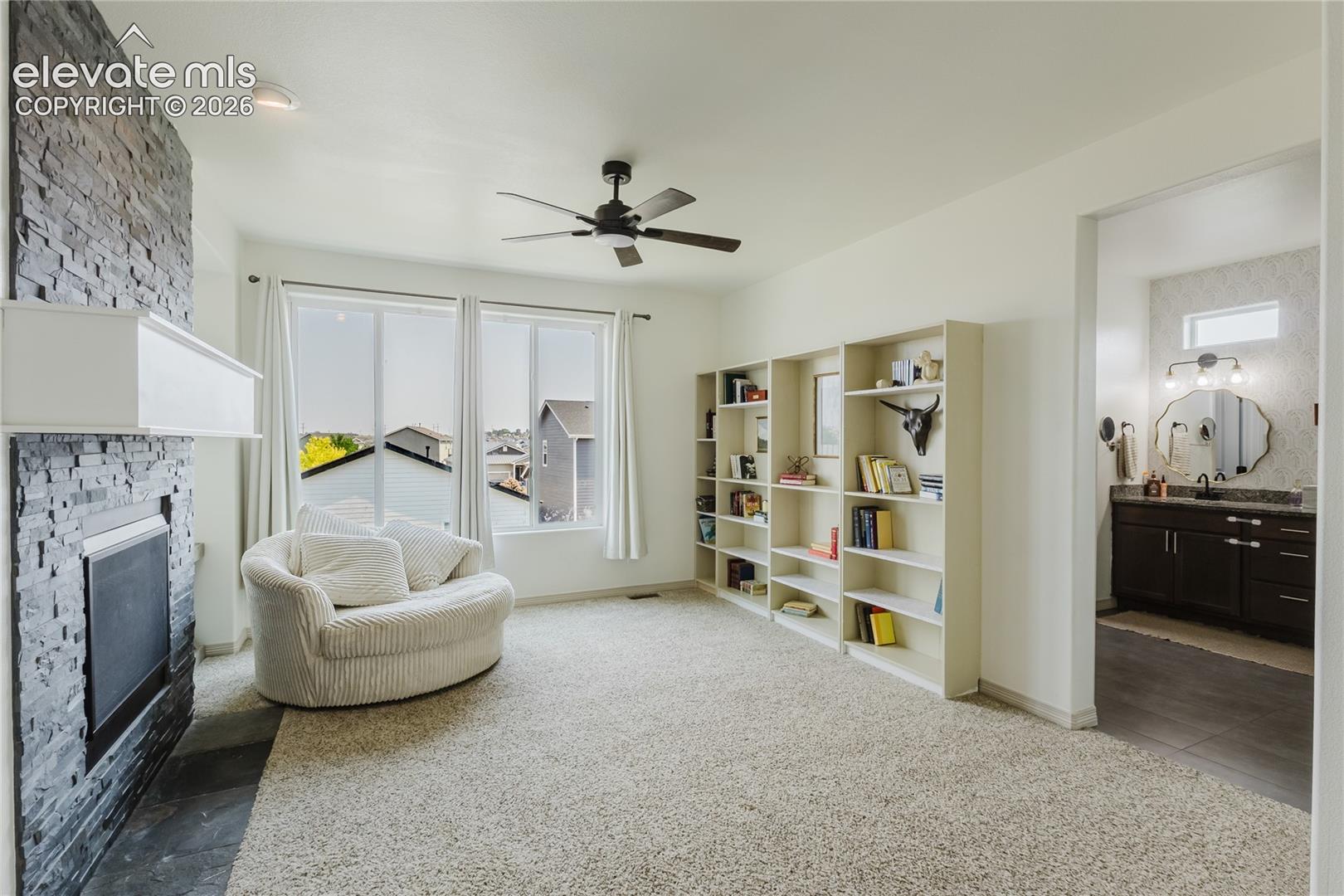 Spacious room featuring a stone-clad fireplace with a white mantel, multiple large windows, and built-in shelving