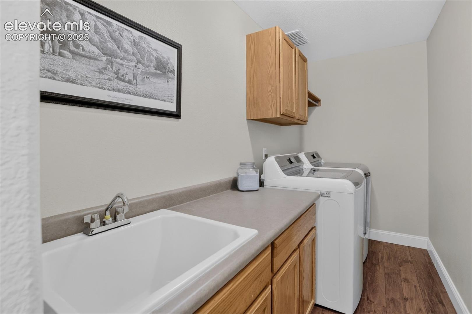Laundry area featuring a utility sink with chrome faucet, light wood-finish cabinetry, and a spacious countertop