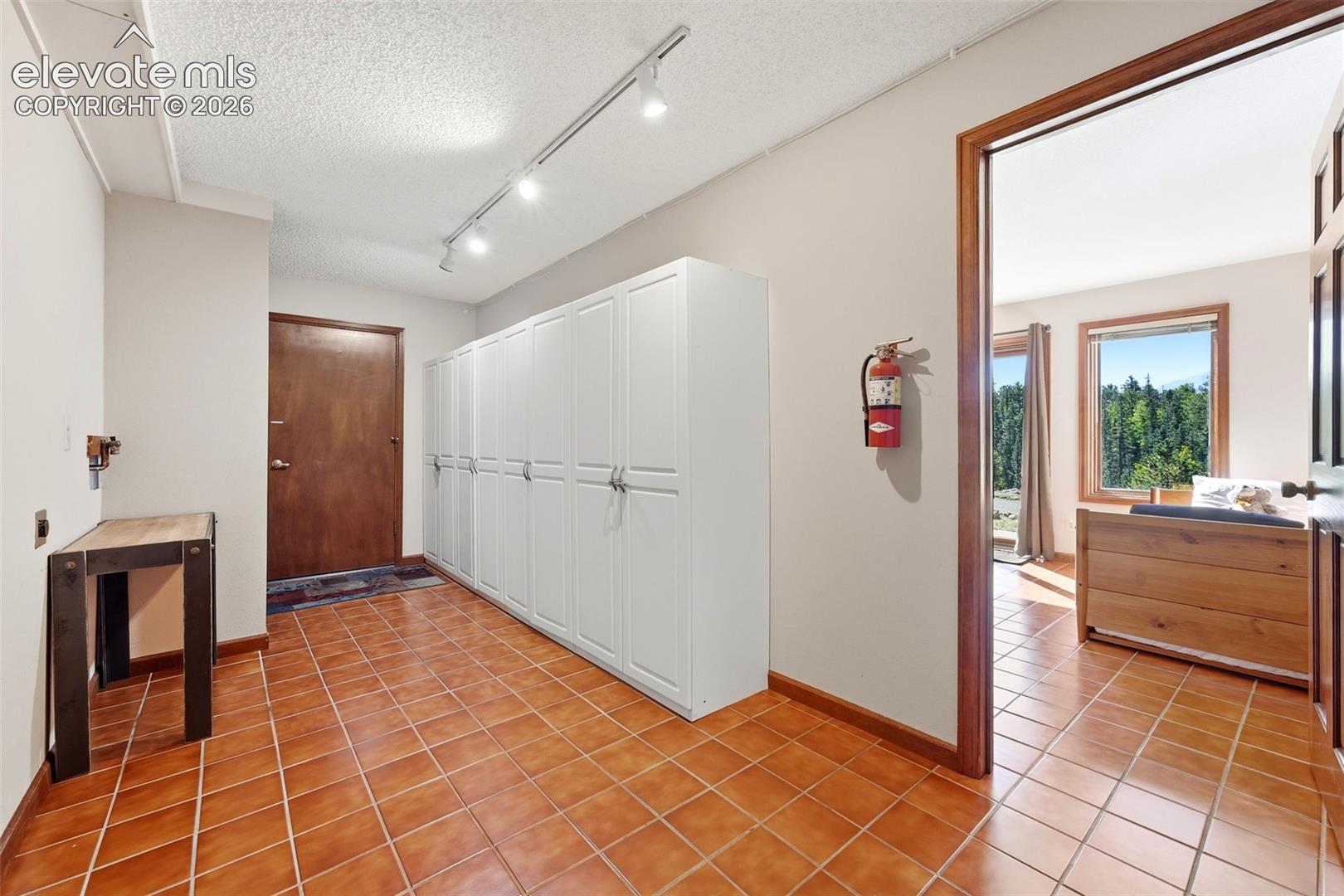 Terracotta tile flooring, extensive built-in white cabinetry, track lighting, and wood-framed doors