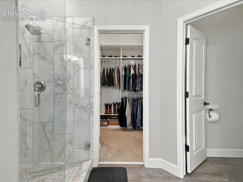 Walk-in shower with clear glass enclosure and marble-look tile surround